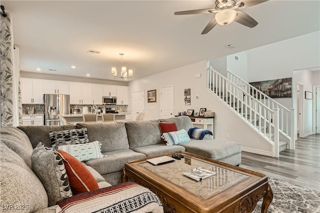 living area with visible vents, stairway, wood finished floors, ceiling fan with notable chandelier, and recessed lighting