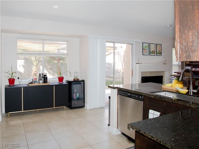 kitchen featuring a tiled fireplace, a sink, dark stone countertops, beverage cooler, and dishwasher