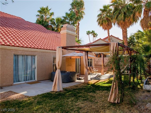 rear view of house featuring a patio, a chimney, a tile roof, and stucco siding