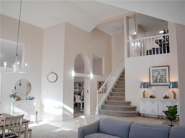 living room with a towering ceiling, tile patterned floors, stairway, and ceiling fan with notable chandelier