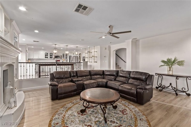 living area featuring ceiling fan, visible vents, light wood finished floors, and arched walkways