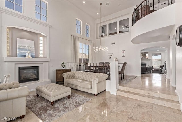 living room with marble finish floor, arched walkways, a high ceiling, baseboards, and a glass covered fireplace