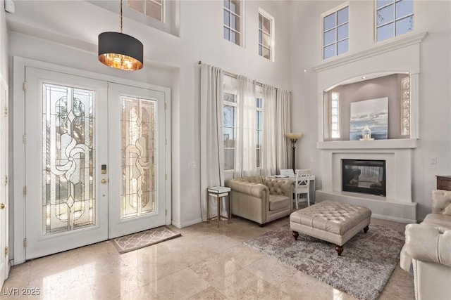 interior space featuring baseboards, french doors, a towering ceiling, and a glass covered fireplace