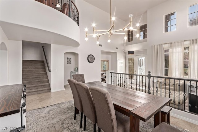 dining area featuring arched walkways, a notable chandelier, a high ceiling, and baseboards