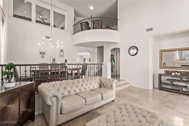 living room with ceiling fan with notable chandelier, visible vents, baseboards, a towering ceiling, and arched walkways