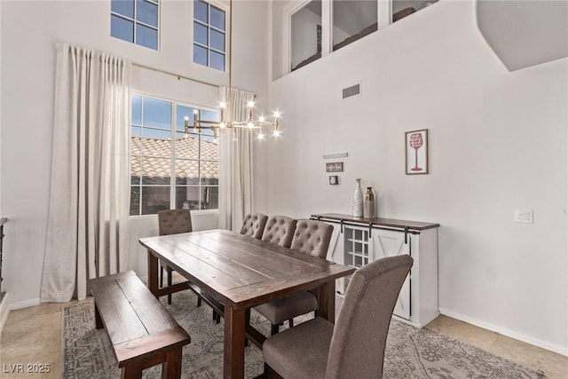 dining space featuring a towering ceiling, baseboards, visible vents, light tile patterned floors, and a notable chandelier