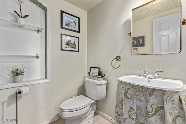 half bathroom featuring toilet, baseboards, and a sink