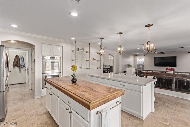 kitchen featuring stainless steel appliances, white cabinets, arched walkways, a kitchen island, and butcher block counters