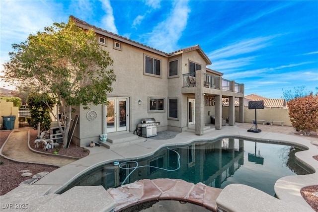 rear view of house featuring french doors, stucco siding, a fenced backyard, a balcony, and a patio area