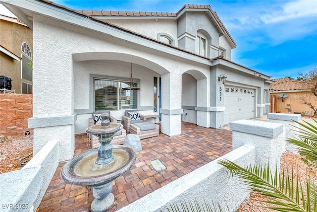 view of front facade featuring a patio area, a tiled roof, an attached garage, and stucco siding