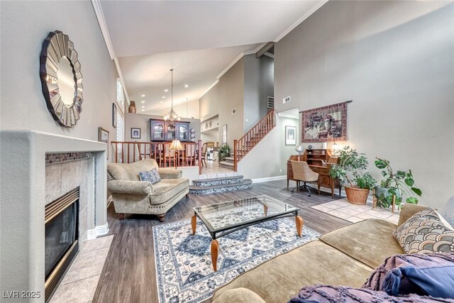 living area with a chandelier, high vaulted ceiling, a tile fireplace, wood finished floors, and ornamental molding