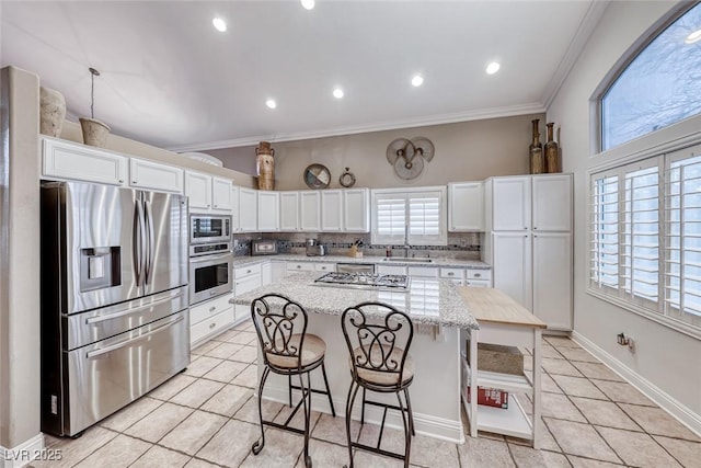 kitchen featuring white cabinets, a breakfast bar area, ornamental molding, stainless steel appliances, and backsplash