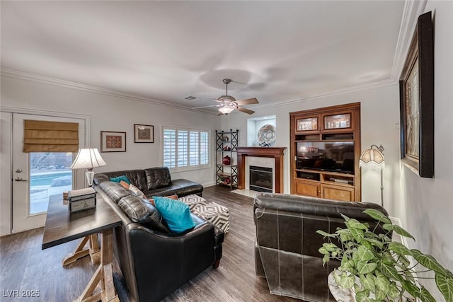 living area featuring ornamental molding, a ceiling fan, a tiled fireplace, and wood finished floors