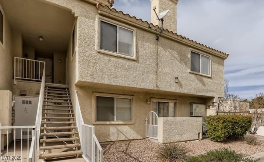 back of property with a tile roof, stairway, and stucco siding