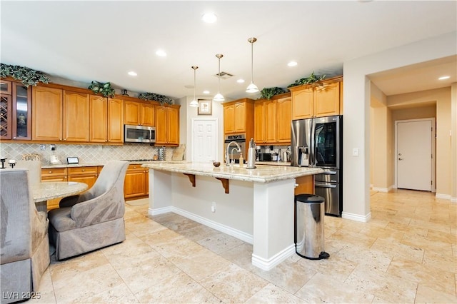 kitchen featuring light stone counters, a breakfast bar area, visible vents, appliances with stainless steel finishes, and backsplash