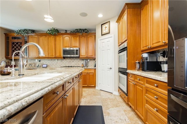 kitchen with stainless steel appliances, tasteful backsplash, a sink, and light stone countertops