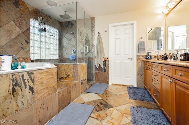 bathroom with a garden tub, vanity, tile walls, a stall shower, and stone tile flooring