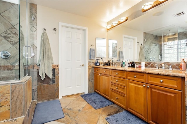 full bathroom with tile walls, double vanity, visible vents, a stall shower, and a sink