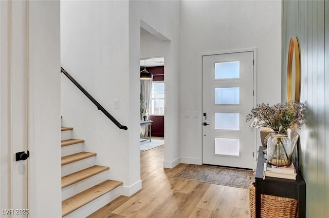 foyer with a high ceiling, stairway, light wood-type flooring, and baseboards