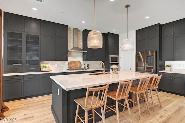 kitchen with wall chimney exhaust hood, appliances with stainless steel finishes, a sink, and light countertops