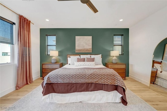 bedroom featuring light wood-type flooring, multiple windows, arched walkways, and baseboards