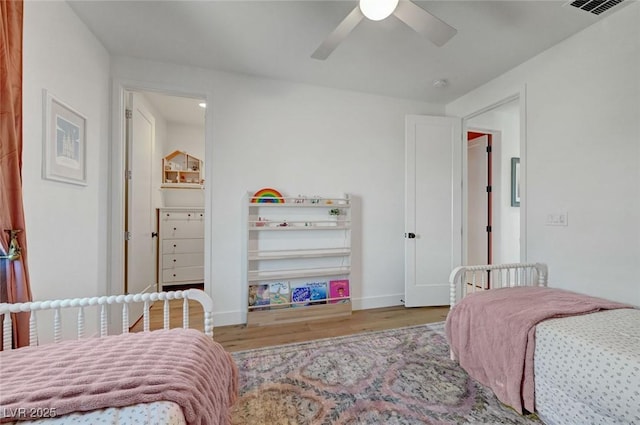 bedroom with ceiling fan, visible vents, baseboards, and wood finished floors