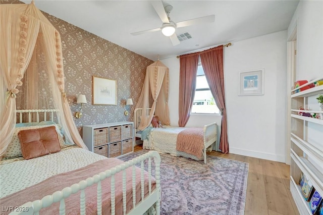 bedroom with visible vents, ceiling fan, wood finished floors, baseboards, and wallpapered walls