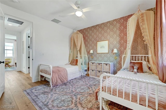 bedroom featuring hardwood / wood-style flooring, visible vents, baseboards, and wallpapered walls