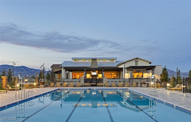 pool at dusk with a mountain view, a patio, a community pool, and fence