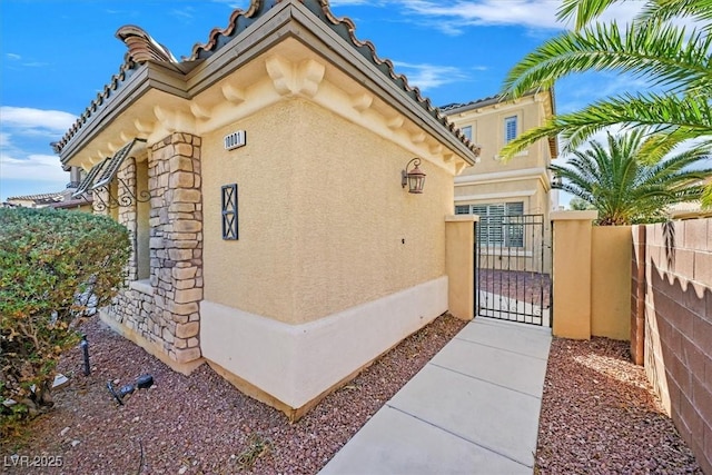 view of side of property featuring stone siding, fence, a gate, and stucco siding