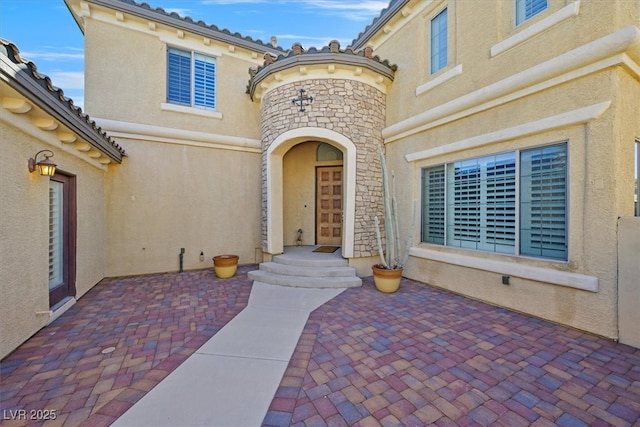 property entrance featuring stone siding, a patio area, and stucco siding