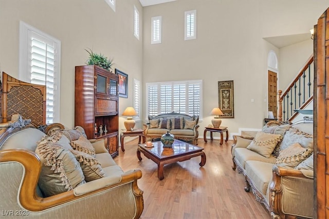 living room with light wood-style floors, plenty of natural light, stairway, and a towering ceiling