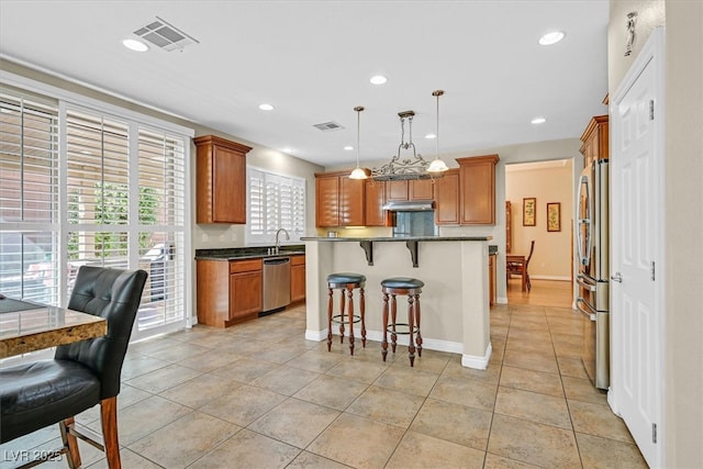 kitchen with a breakfast bar area, stainless steel appliances, visible vents, a sink, and under cabinet range hood