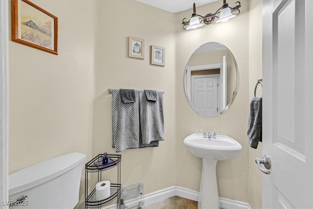 half bathroom with toilet, baseboards, and a sink