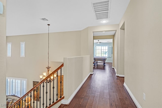 hall with dark wood-style floors, an upstairs landing, visible vents, and baseboards