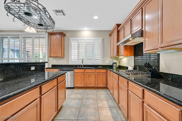 kitchen with visible vents, dark stone countertops, stainless steel appliances, under cabinet range hood, and a sink