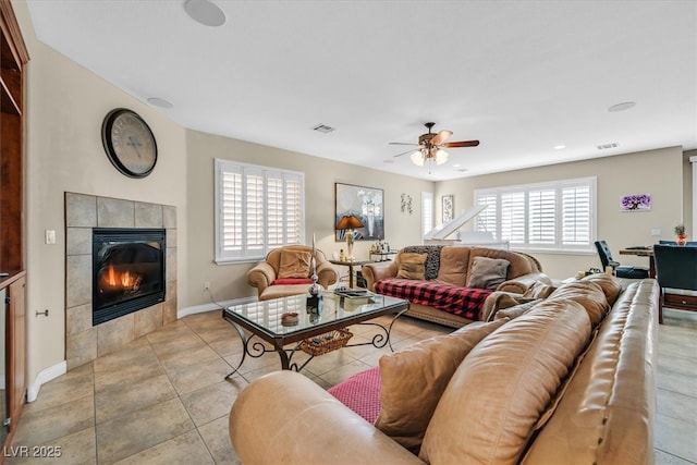 living room featuring light tile patterned floors, ceiling fan, a tile fireplace, visible vents, and baseboards