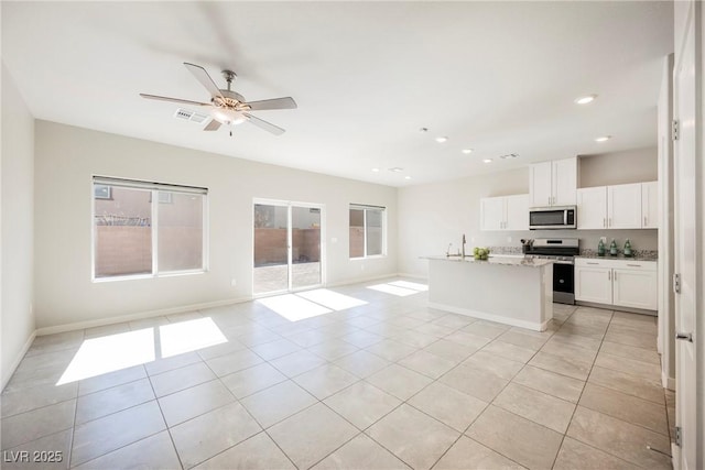 kitchen with a ceiling fan, white cabinets, open floor plan, appliances with stainless steel finishes, and a center island with sink