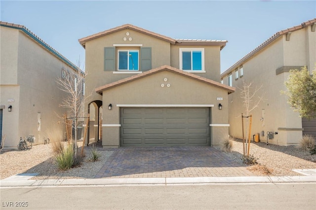 view of front of home with decorative driveway, an attached garage, a tile roof, and stucco siding