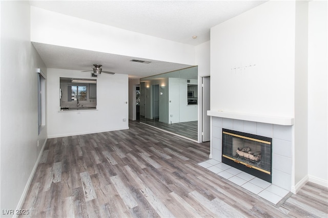 unfurnished living room featuring a tile fireplace, wood finished floors, visible vents, baseboards, and a ceiling fan