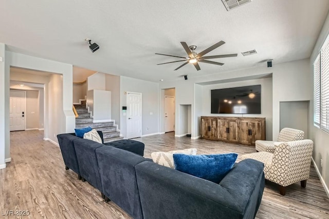 living area with wood finished floors, visible vents, baseboards, and stairs