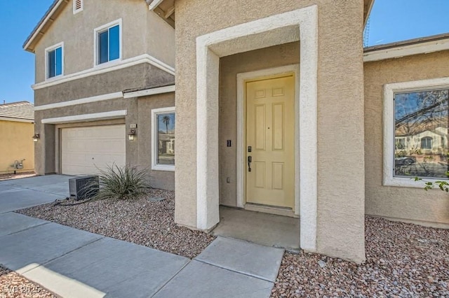 entrance to property featuring a garage, concrete driveway, and stucco siding