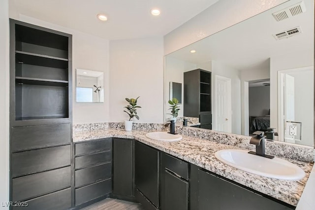 ensuite bathroom with double vanity, connected bathroom, visible vents, and a sink