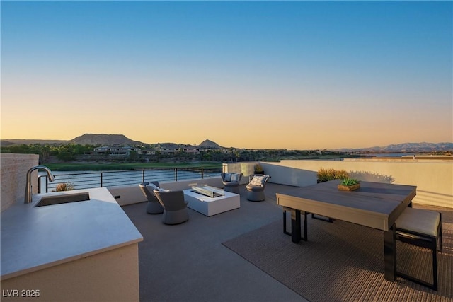 patio terrace at dusk featuring a fire pit, outdoor dining area, a sink, and a water and mountain view