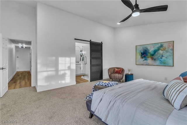 bedroom with connected bathroom, baseboards, ceiling fan, a barn door, and carpet flooring