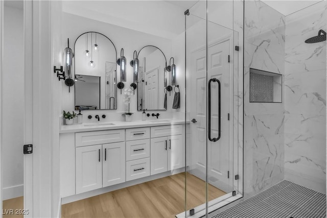 full bathroom with a marble finish shower, double vanity, wood finished floors, and a sink