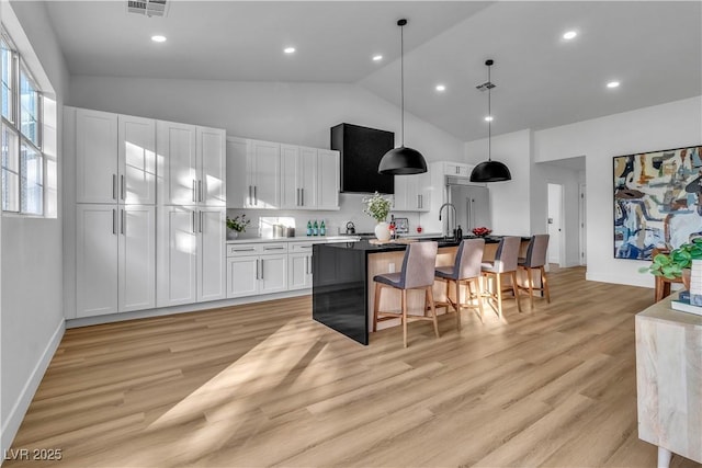 kitchen with light wood finished floors, a center island with sink, a breakfast bar, hanging light fixtures, and white cabinetry