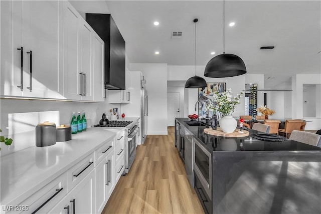 kitchen featuring light wood finished floors, a sink, stainless steel stove, white cabinets, and wall chimney range hood