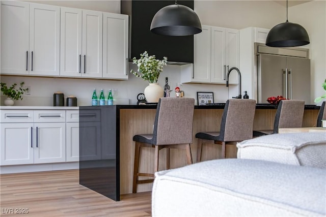 kitchen featuring pendant lighting, high end fridge, light wood-style floors, a breakfast bar area, and white cabinets