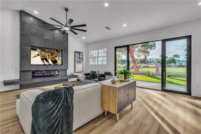 living area featuring visible vents, recessed lighting, vaulted ceiling, a tiled fireplace, and light wood-type flooring